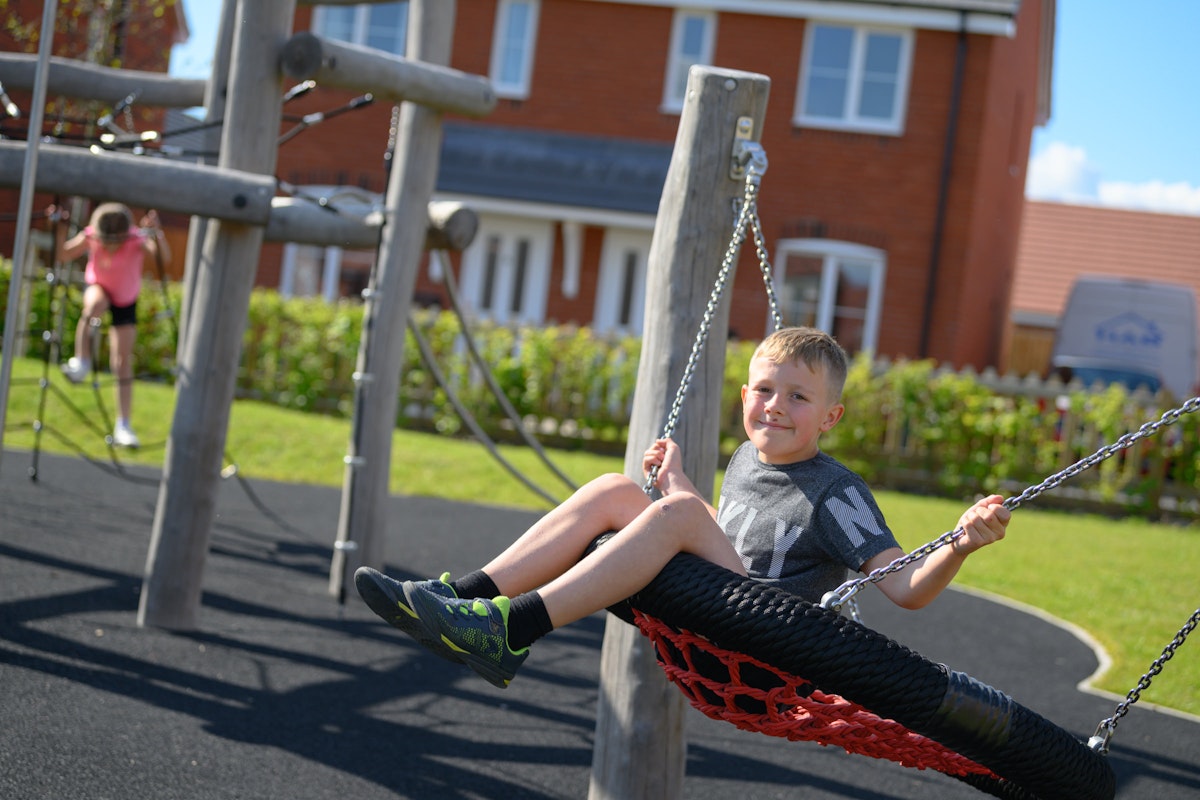 A boy swinging on a swing at a park outside a new housing development